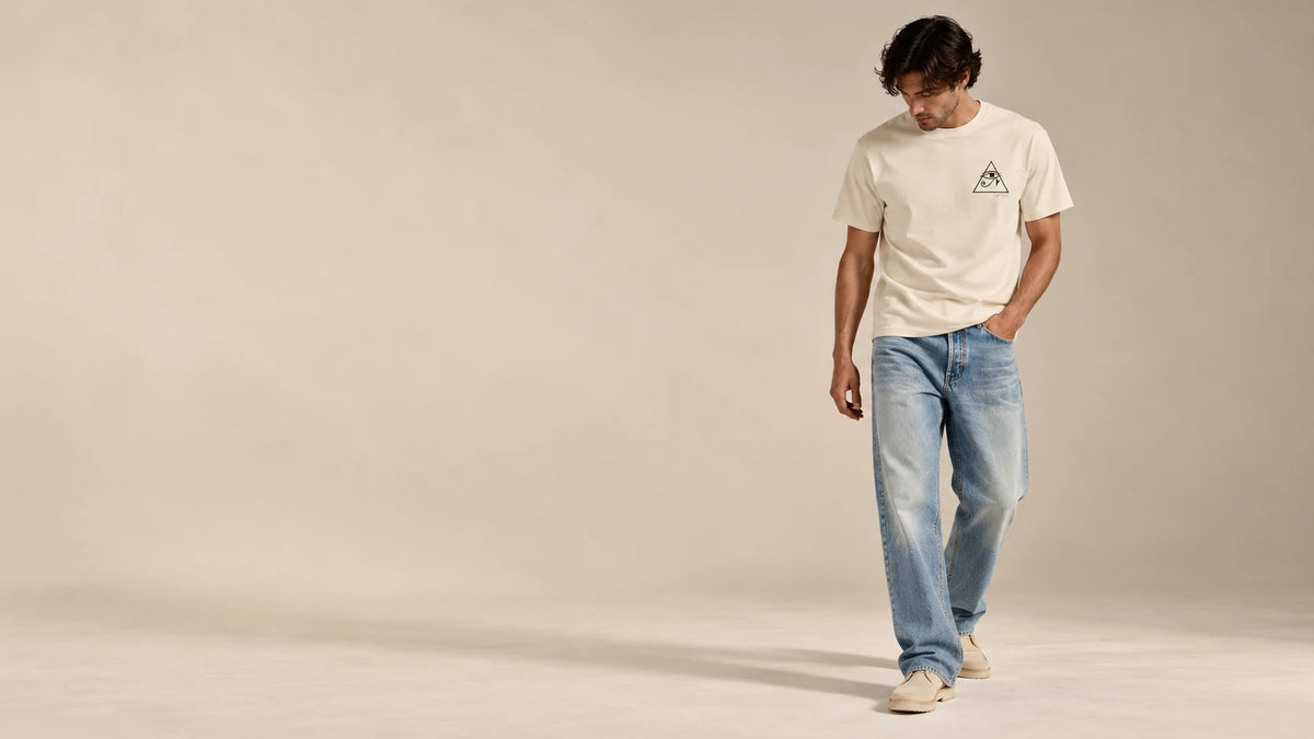 Fictional model wearing the soft cream GFTD MNDS tee with blue jeans in a warm studio